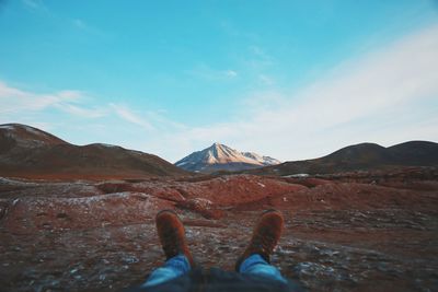 Low section of person standing on mountain against blue sky