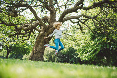 Full length of mid adult woman jumping against tree in field