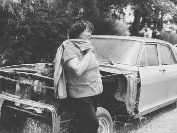 Smiling woman standing by abandoned car