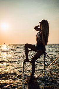 Woman sitting by sea against sky during sunset