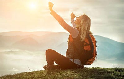 Rear view of woman sitting on field against sky during sunset