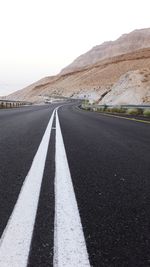 Road leading towards mountain against clear sky