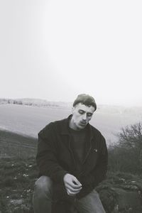 Portrait of young man sitting on landscape against clear sky