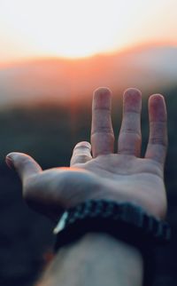 Close-up of human hand against sky during sunset