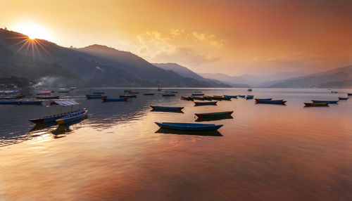 Sailboats moored on sea against sky during sunset