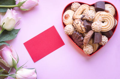 Close-up of flowers with chocolate in heart shape against pink background