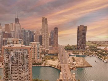 Modern buildings by river against sky during sunset