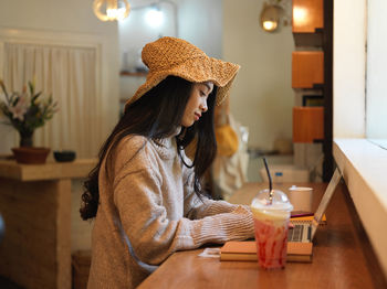 Young woman working on laptop by milkshake at cafe