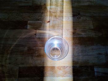 High angle view of glass on wooden table in sunlight beam
