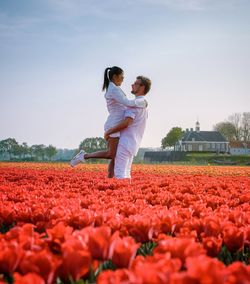 Side view of man carrying girlfriend while standing amidst tulip flowers