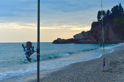 Fishing rods at beach against sky during sunset