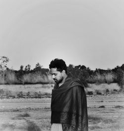 Portrait of young man standing on field against clear sky