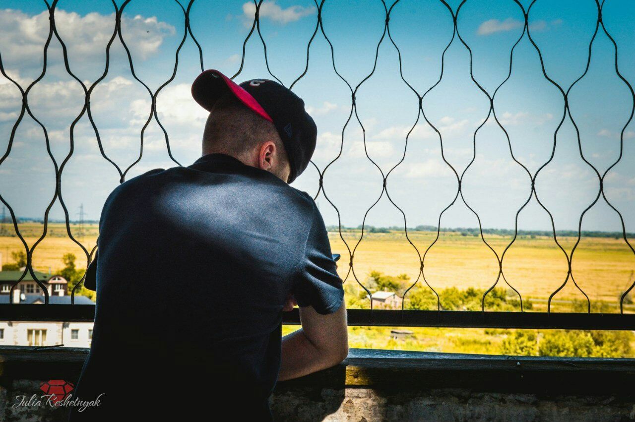 lifestyles, rear view, standing, leisure activity, fence, three quarter length, focus on foreground, chainlink fence, men, waist up, sky, casual clothing, person, protection, sitting, railing, field, looking away