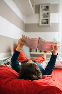 Boy reading book while lying on bed at home
