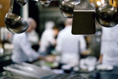 Ladles and spatula hanging against men working in kitchen