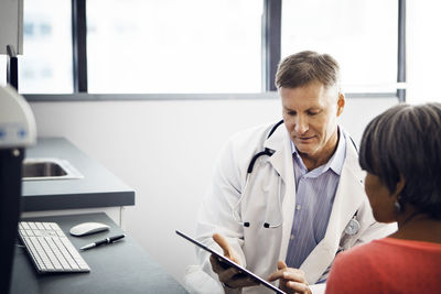 Male doctor showing report on tablet computer to patient in clinic