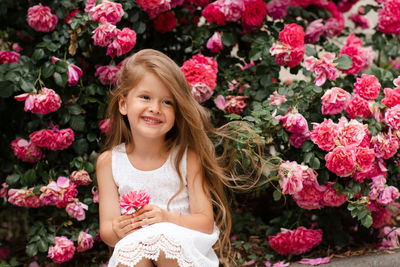 Cute baby girl 5-6 year old hold rose flower sit over bloom bushes in garden outdoor. spring season