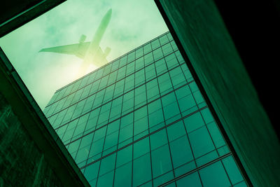 Bottom view modern glass office building with an airplane flying above building. exterior facade 