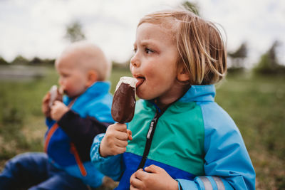 Young male kids looking to side licking chocolate popsicle ice cream