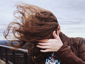 Close-up of woman with brown tousled hair against sky