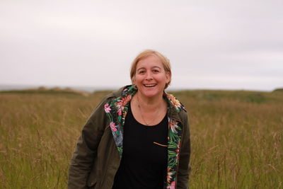 Smiling young woman standing on field against sky