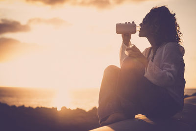 Side view of woman photographing at sunset