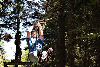 Full length of senior man zip lining in forest