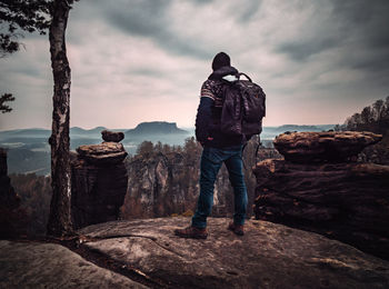 Rear view of man standing on rock against sky