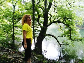 Young woman standing by tree trunk in forest