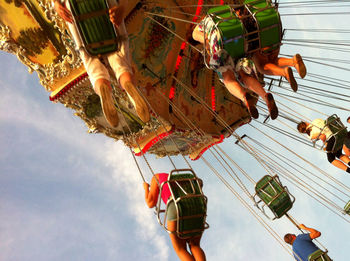 Low angle view of people in chain swing ride against sky