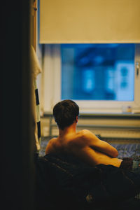 Rear view of shirtless man sitting outdoors