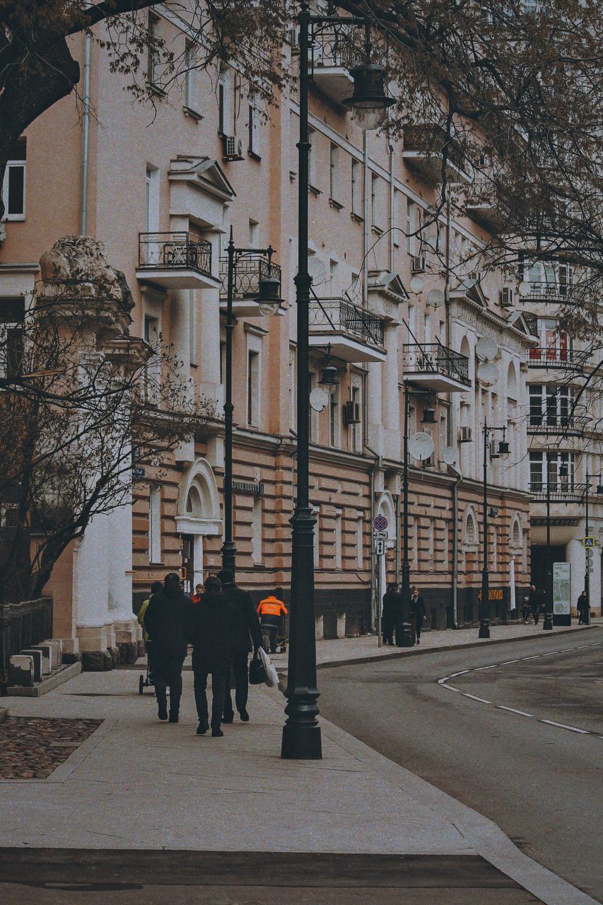 REAR VIEW OF PEOPLE WALKING ON STREET BY BUILDINGS