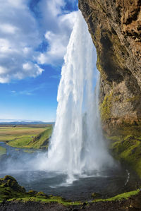 Close-up of seljalandsfoss flowing from mountain against cloudy blue sky