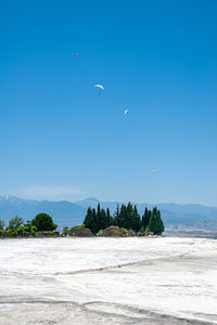 Paragliders flying above white travertines of pamukkale in an ancient city of hierapolis in turkey.