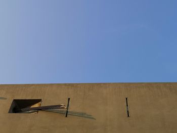 Low angle view of metallic wall against clear blue sky