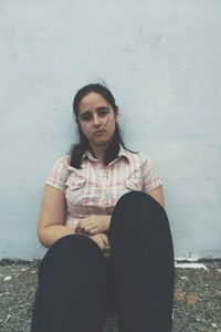 Portrait of young woman sitting against wall