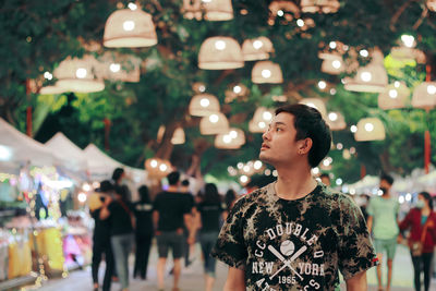 Man looking away while standing against illuminated lights