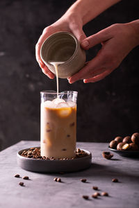 Woman pouring milk into a glass with iced coffee