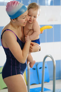 Early age swimming in pool. baby boy waiting near side on mothers hands.happy child with coach woman