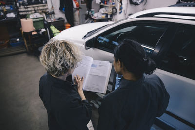 Female mechanic explaining coworker over diary in auto repair shop