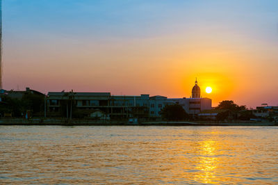 Buildings by sea against sky during sunset