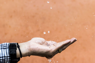 Close-up of water drops falling on hand against wall