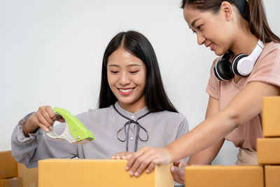 Portrait of smiling young woman using mobile phone while standing against white background