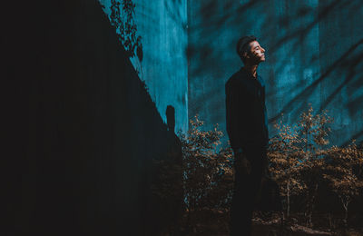 Side view of young man standing against blue wall