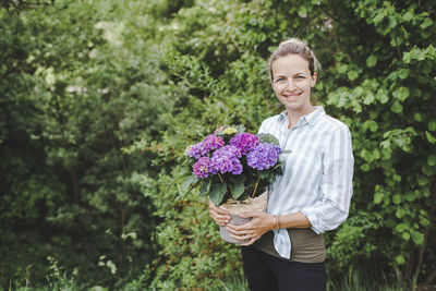 Portrait of smiling young woman standing against plants