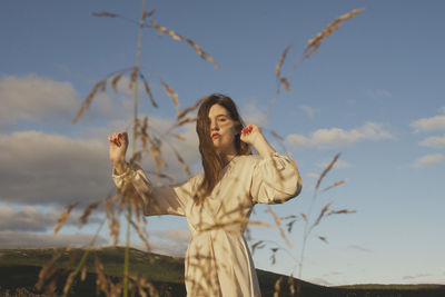 Young woman standing by tree on field against sky