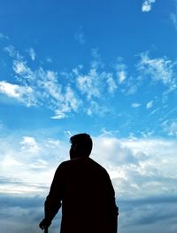 Rear view of silhouette man standing against blue sky