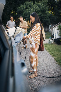 Side view of mature woman charging car with electric plug in back yard