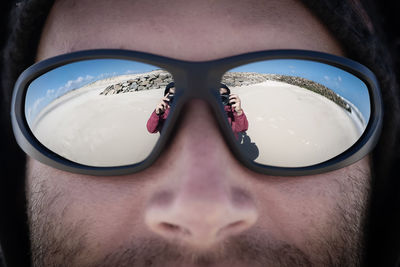 Cropped image of man with woman at beach reflection in sunglasses