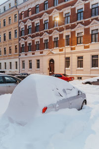 Snow covered street and cars amidst buildings in city